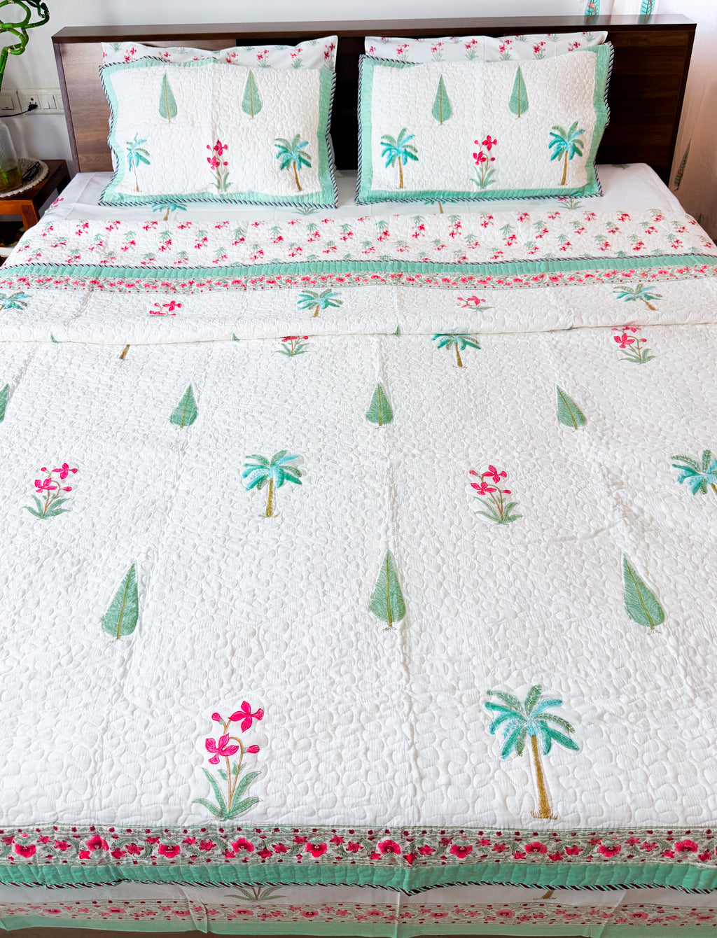 Palm and Pink Floral quilted bedcover styled on a bed, showing palms, pink flowers and mint border.