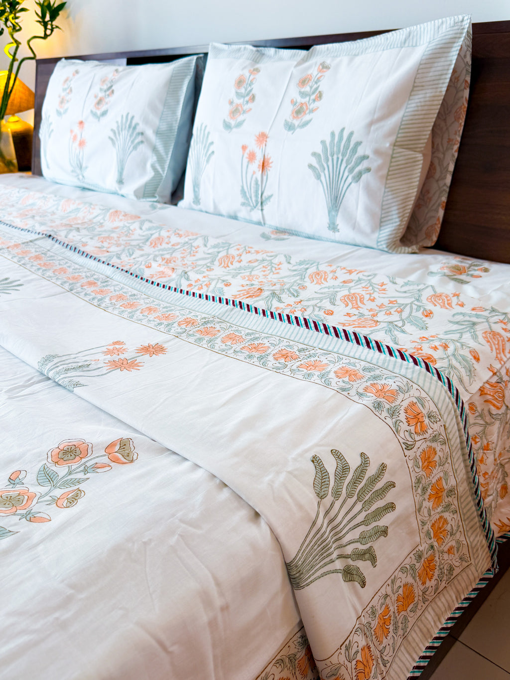 Angled bed view of the Orange Floral and Green Leaf hand-block dohar with orange floral and green botanical motifs.