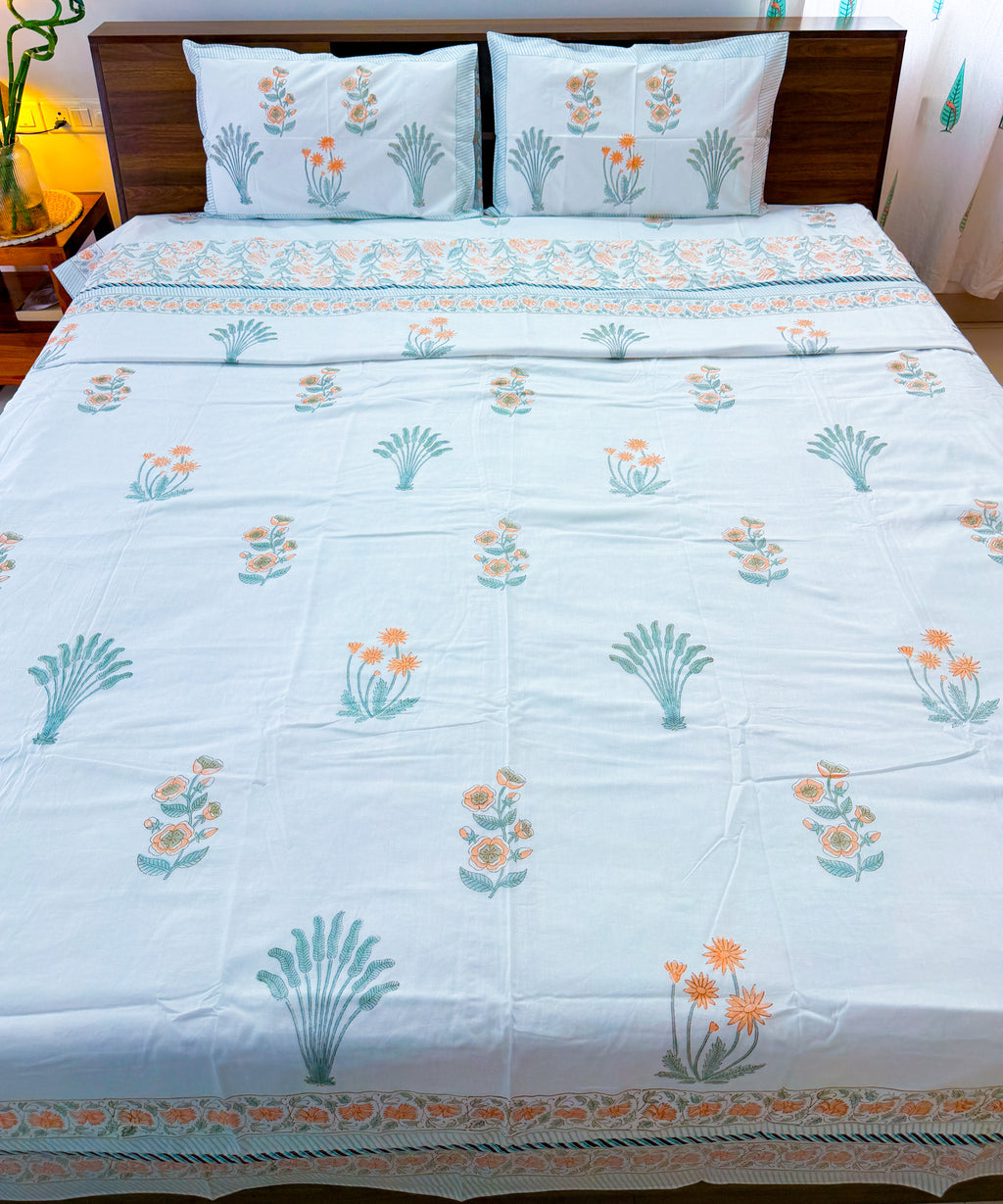 Full bed view of the Orange Floral and Green Leaf hand-block dohar, showing the ivory field and printed border.